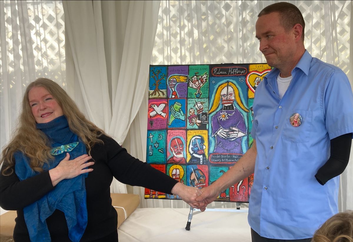 Presents his painting “Ode to Rebecca Hoffberger” to AVAM’s founding director at the museum, Baltimore, 2022: photograph 3 (Posted by Matt Sesow on Facebook, April 18, 2022)