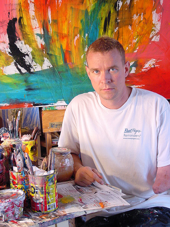 Brushes in coffee cans, the paint-crusted table, a new canvas behind him.